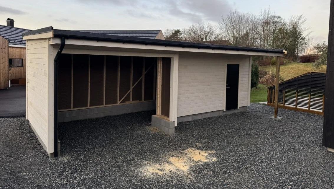 Garasje med integrert carport og bod i moderne stil på gruslagt uteområde.