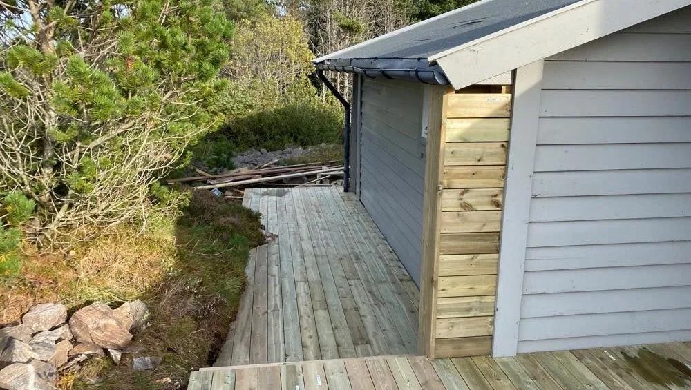 Treterrasse langs husvegg med ny kledning, omgitt av natur og stein i rolig uteområde.